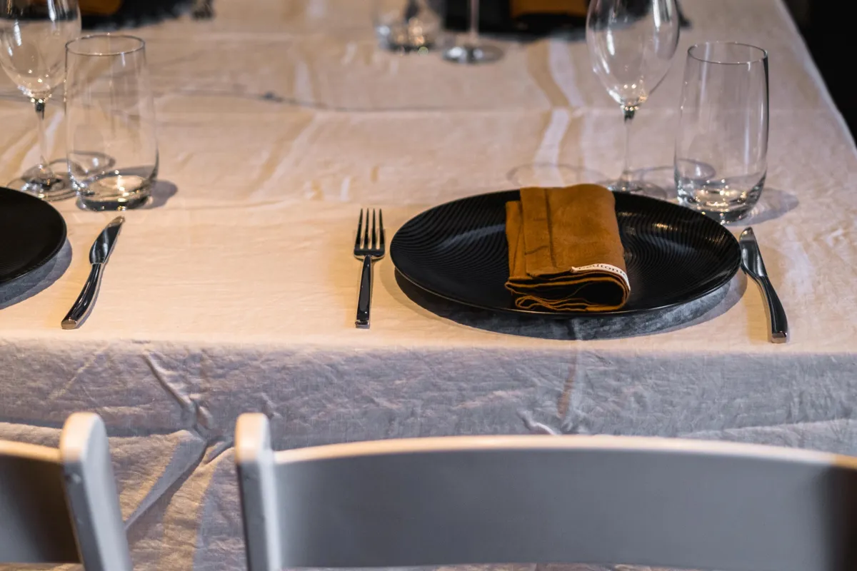 Brown napkin on dark plates beside glasses on a white tablecloth