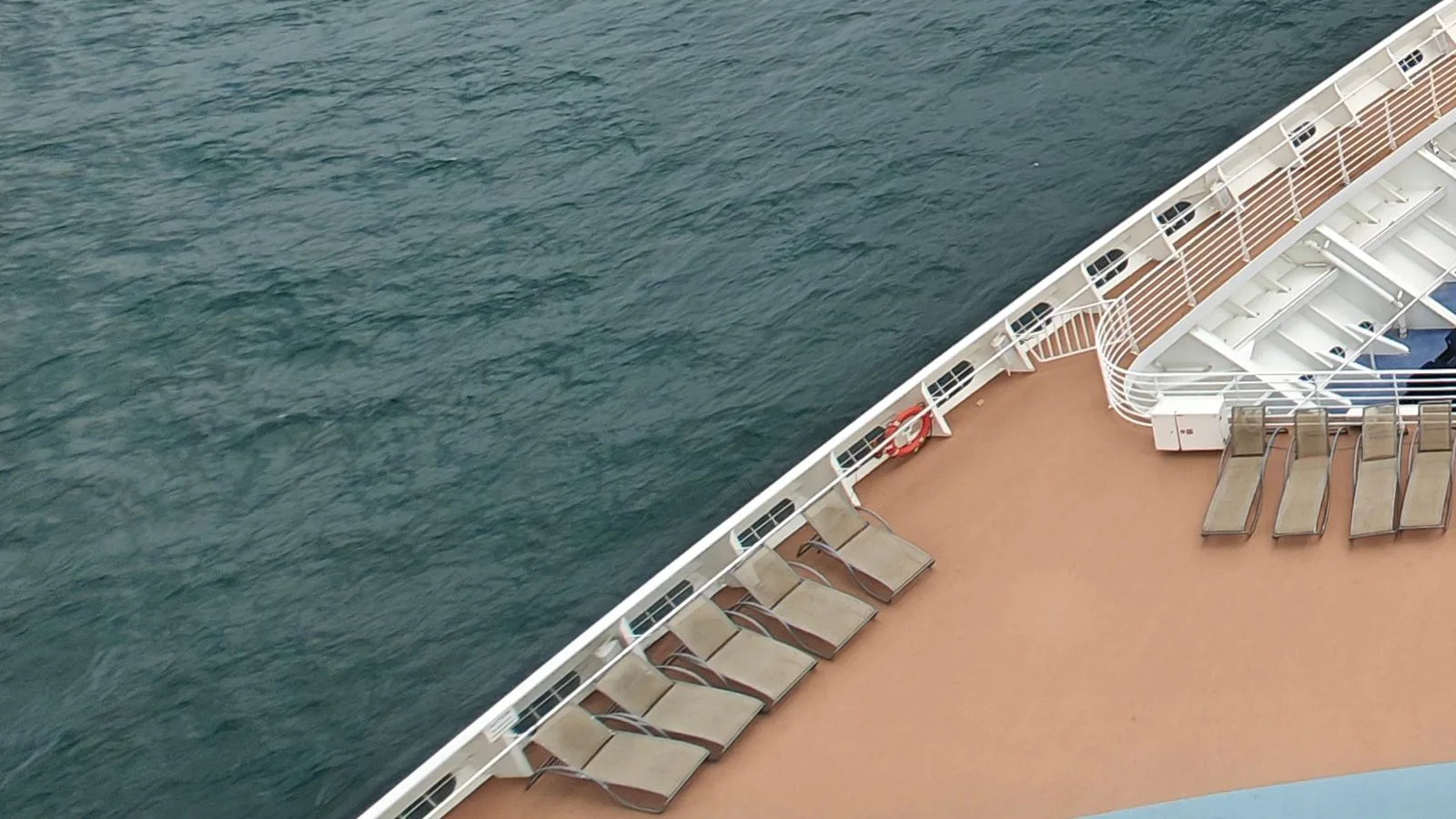 Empty loungers beside a ship railing overlooking blue-green ocean